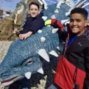 Two boys smiling beside blue dinosaur statue